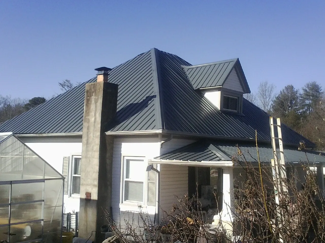 Dark blue standing seam metal roof on a white farmhouse with dormer — Slate & Tile Roof Repair by Roofing Brothers in Gratiot