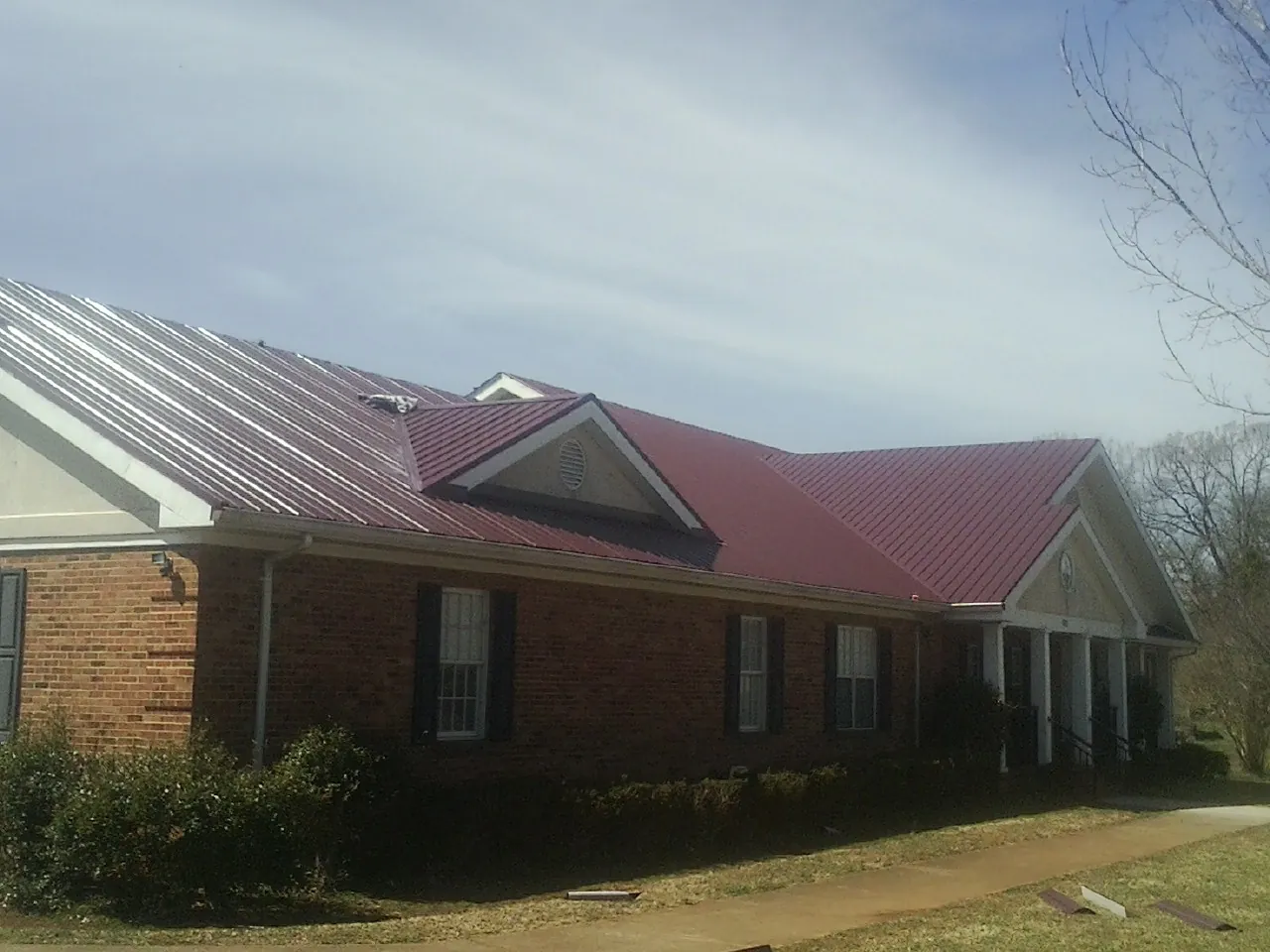 Red metal roof with gabled entries on a long brick building, from a Hail Damage Roof Repair job in Gratiot