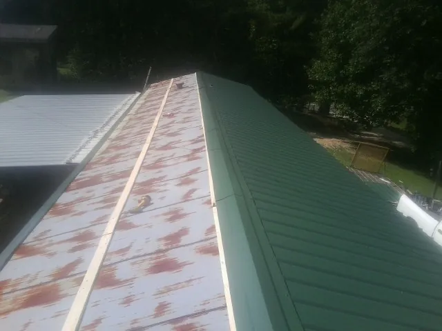 Old rusted panels beside newly installed green metal roofing — Wind Damage Roof Repair by Roofing Brothers in Gratiot