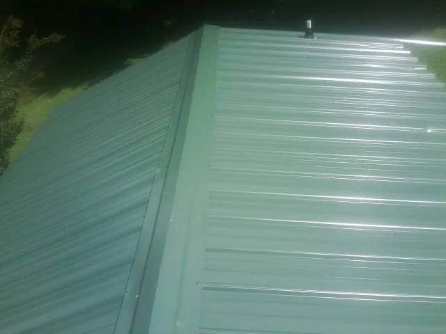 New green metal panels meeting at the ridge of a roof — Flat Roof Repair work by our crew in Gratiot