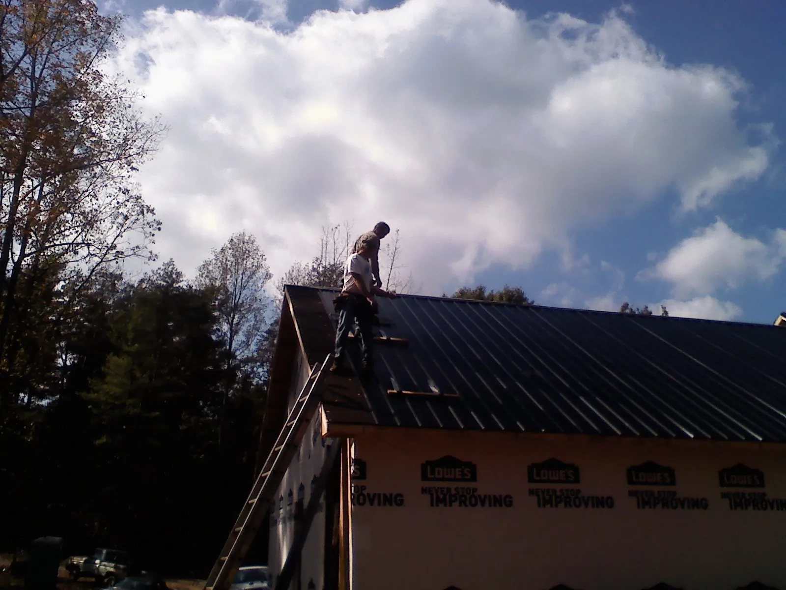 Roofer fastening dark metal panels high against a cloudy sky, from a Roof Inspection job in Gratiot