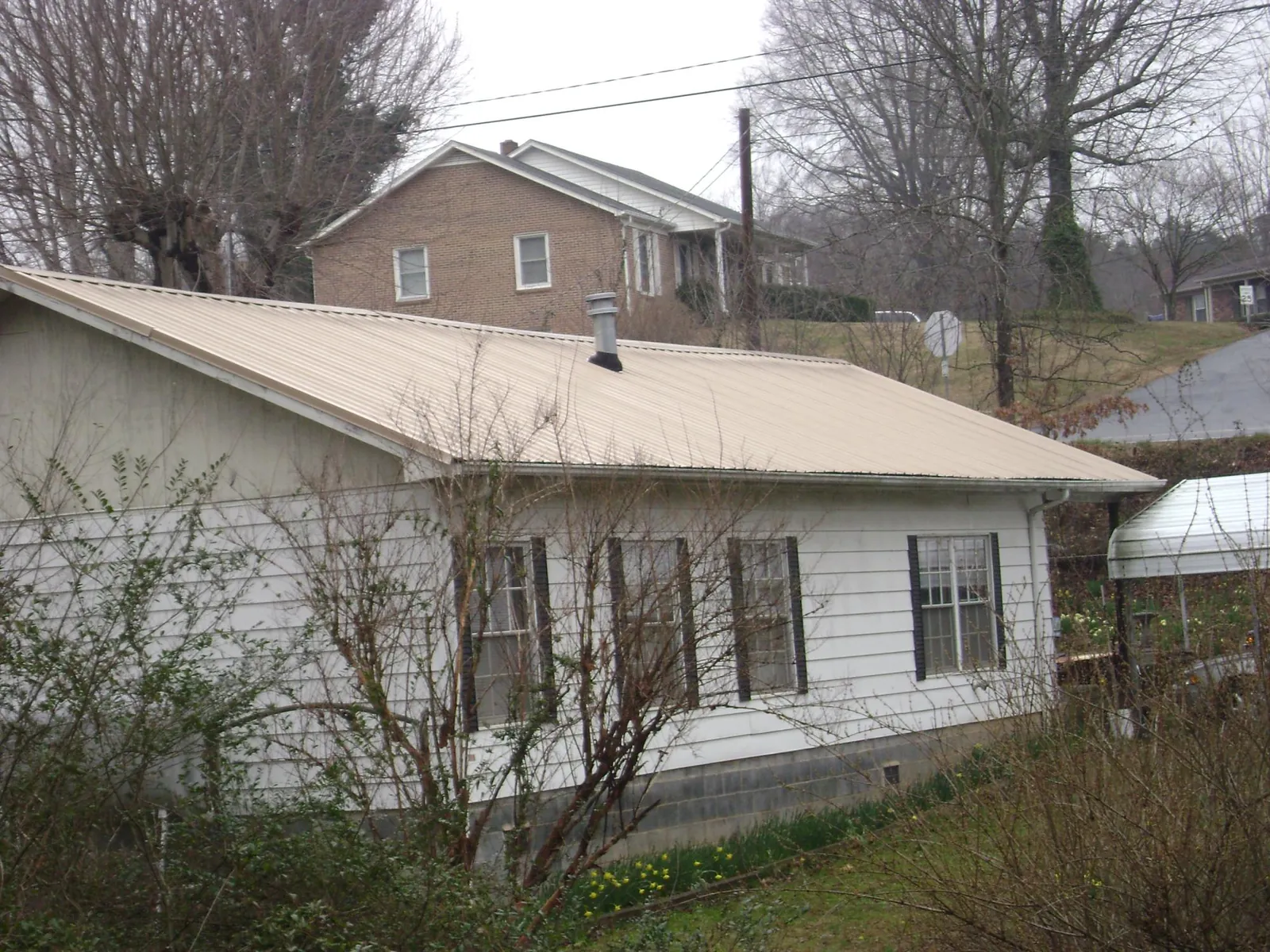 Tan metal roof on a white sided house set into a hillside — Commercial Roofing by Roofing Brothers in Gratiot