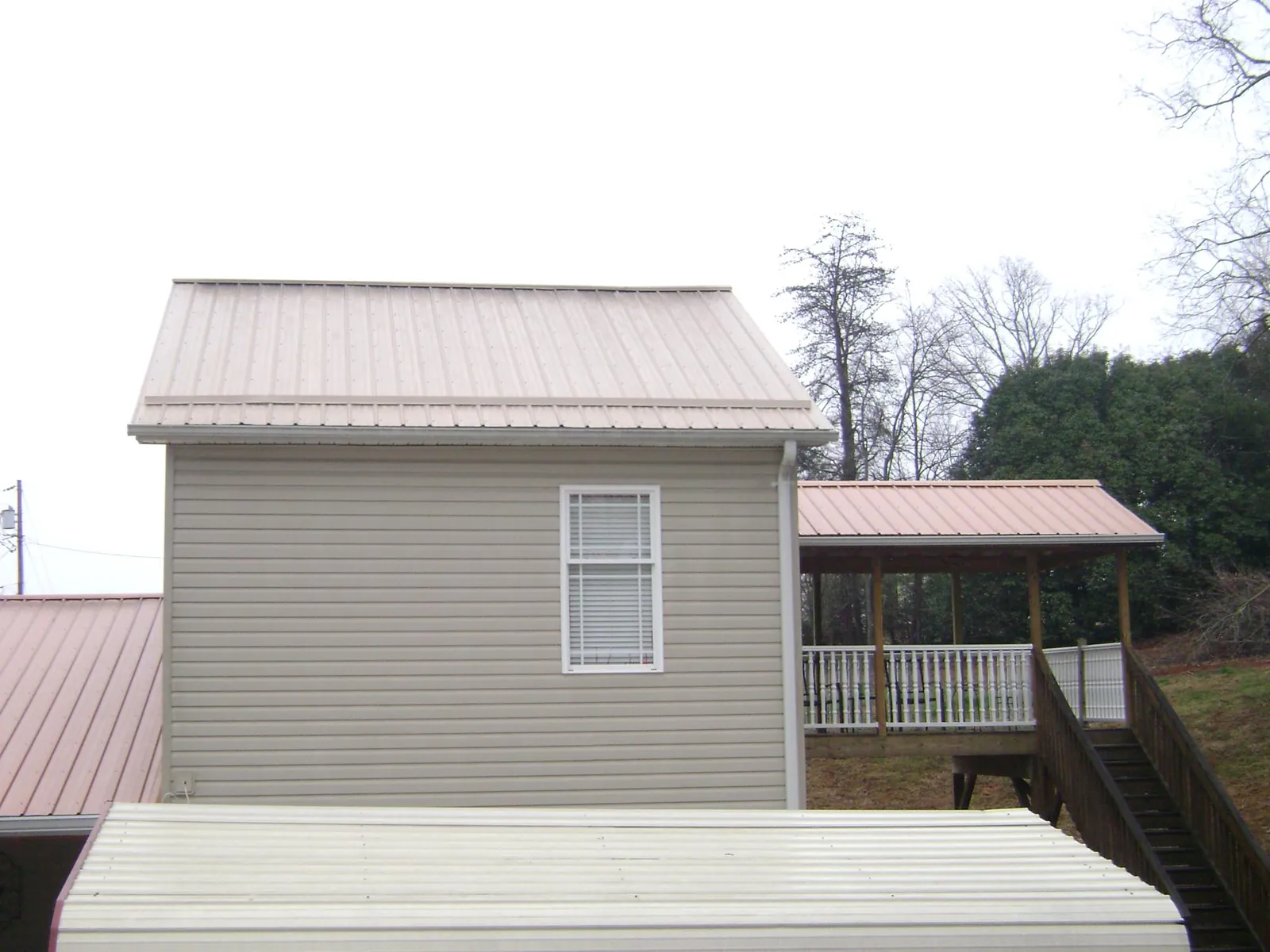 Tan metal roofs on a two story addition and attached porch, from a Roof Replacement job in Gratiot